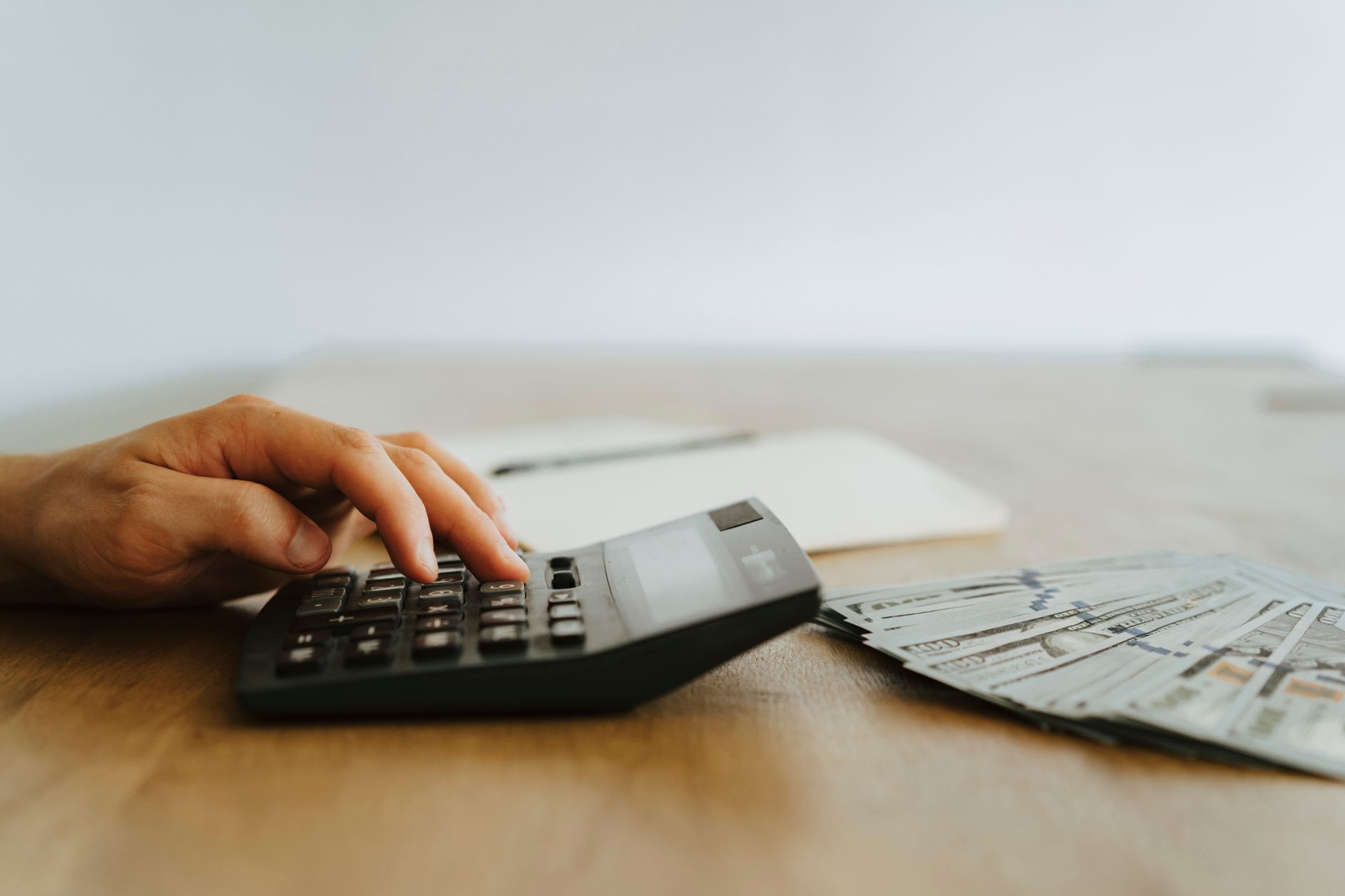 Mão calculando finanças com calculadora ao lado de notas de dinheiro